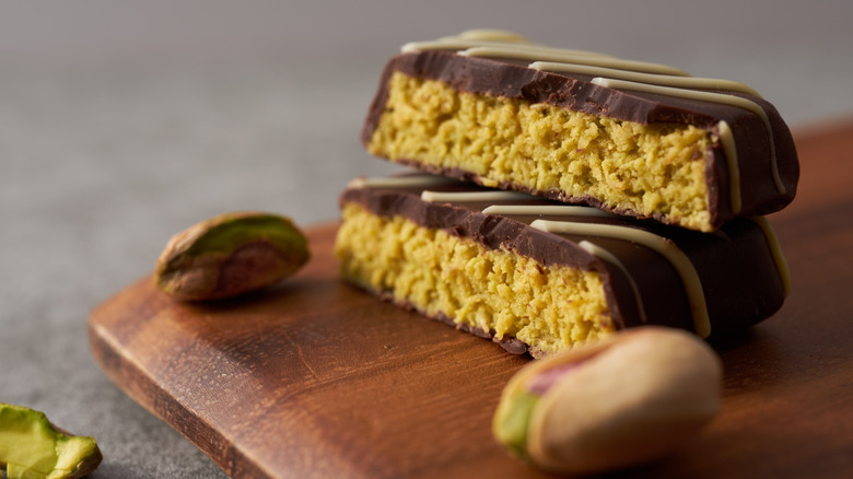 A Dubai chocolate bar split in half on a wooden board beside a few pistachios