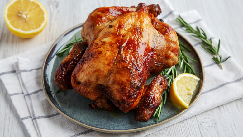 A rotissiere chicken on a plate with lemons near an herb sprig