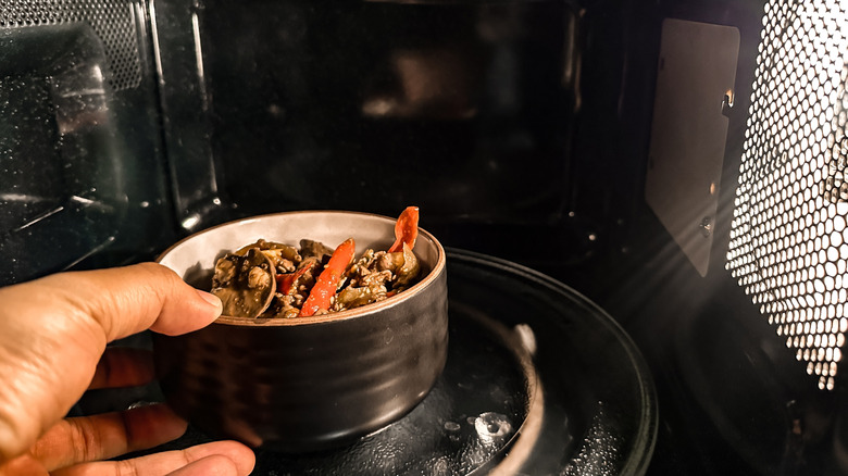 A hand places a bowl of food in a microwave