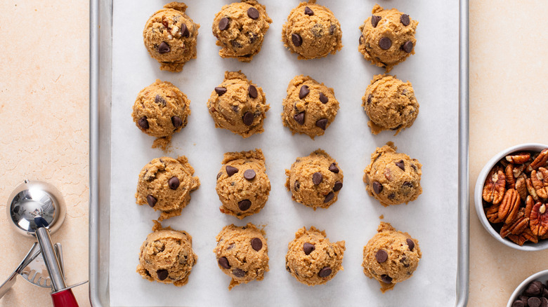 Scoops of chocolate chip cookie dough on parchment-lined sheet pan