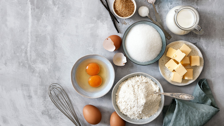 Top view of assorted baking ingredients including eggs, butter, sugar, flour, and milk