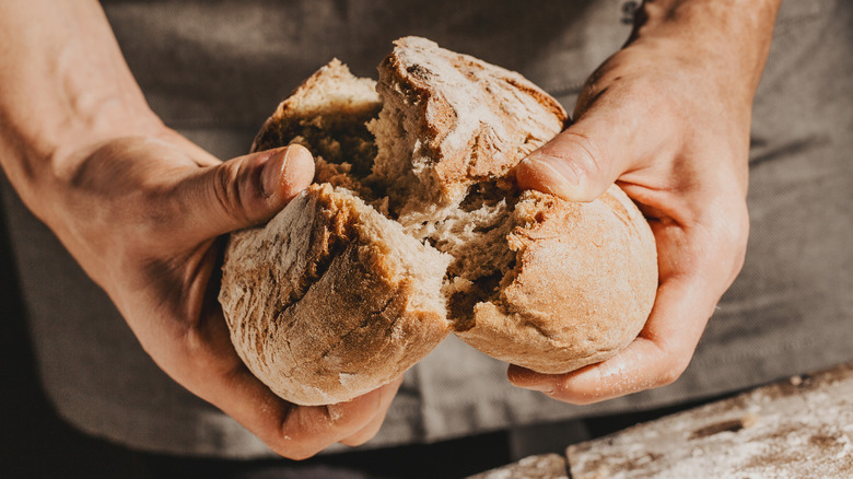 Person breaking flat boule of bread in half