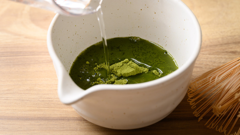 Water being poured into matcha powder in a white bowl