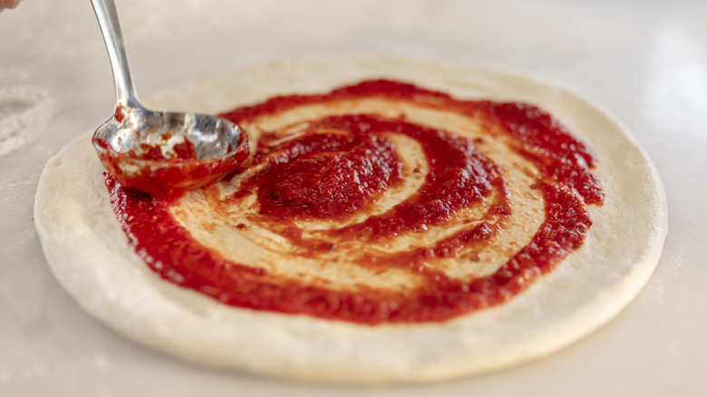spreading red sauce on dough