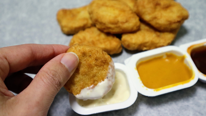 Hand dipping chicken nugget in trio of sauces