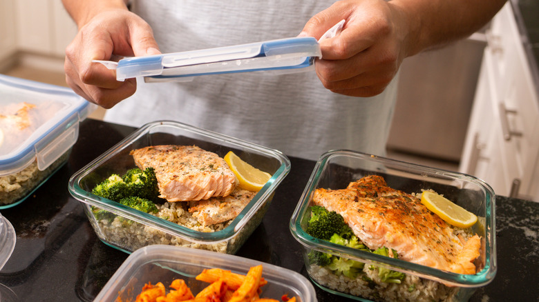 A person placing a lid on top of a glass container with salmon and veggies inside.