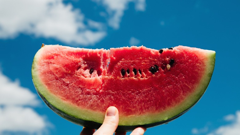A slice of watermelon being held up to the sky.