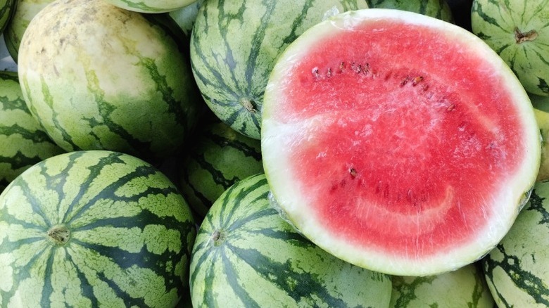 Several watermelons in a pile, with one cut open.