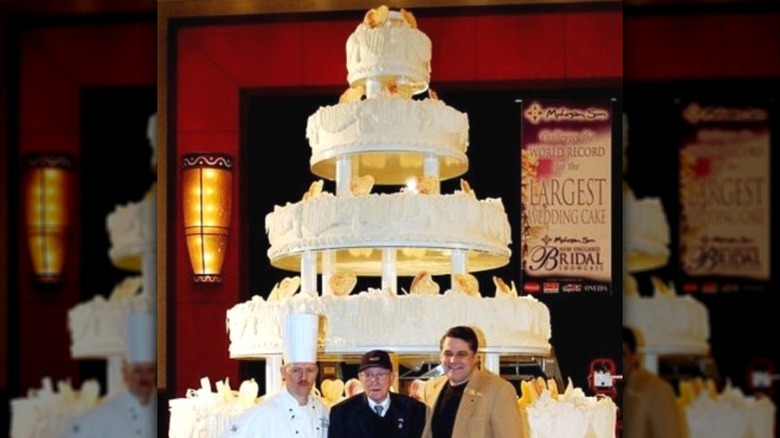 Three men standing in front of the world's largest wedding cake.