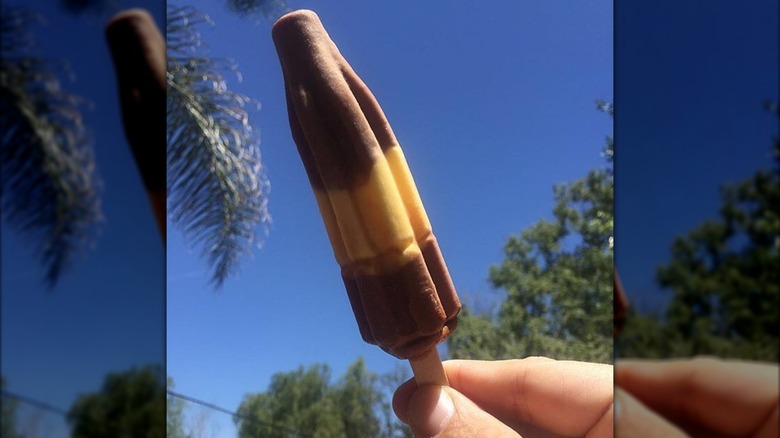Hand holding banana fudge popsicle against sky