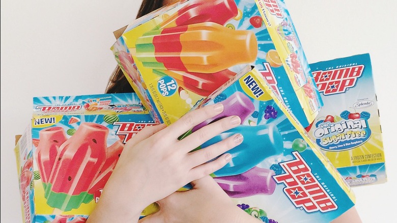 hands holding various boxes of bomb pops