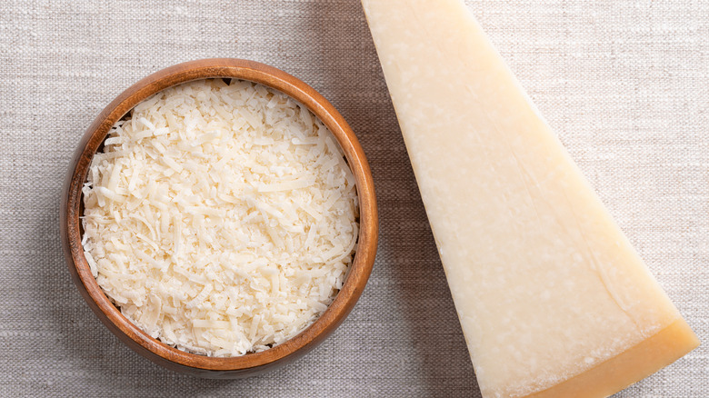 bowl of grated parmesan next to a parmesan wedge