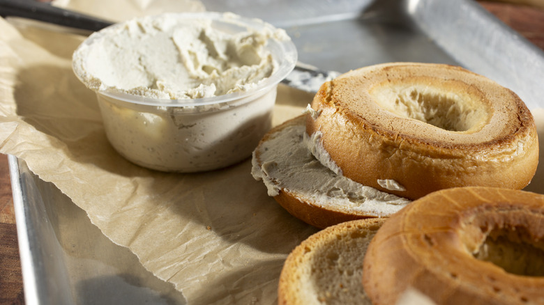 A container of cream cheese next to gluten free bagels.