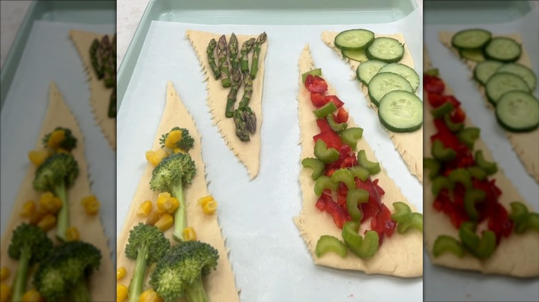 Rolled out crescent rolls topped with various vegetables on a lined baking sheet