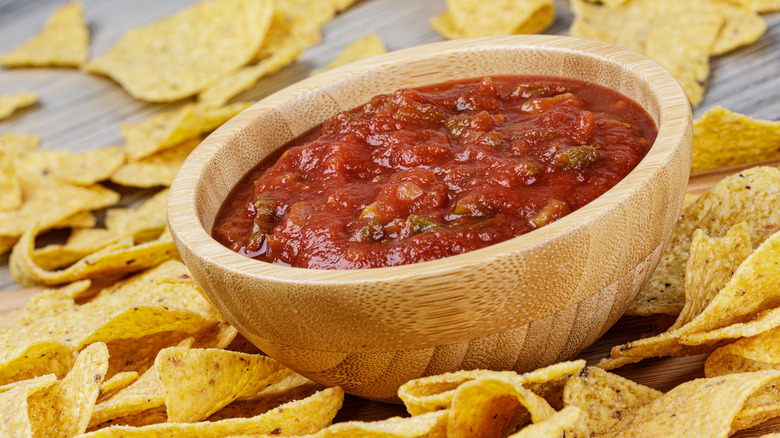A large wooden bowl of Salsa with tortilla chips on a wooden board.