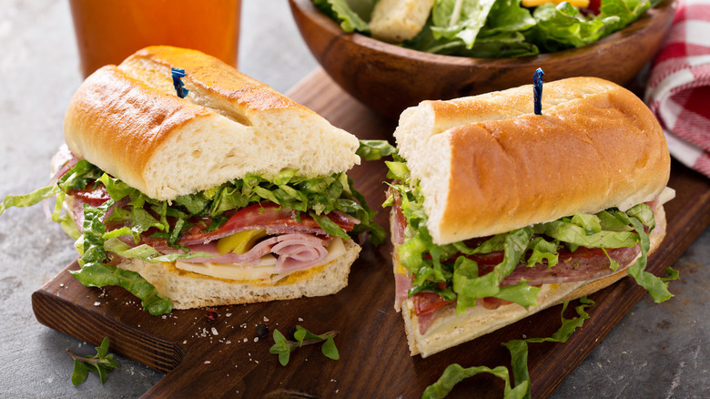 Italian sandwich with meat and veggies cut in half on a wood serving platter near a salad and a beer.