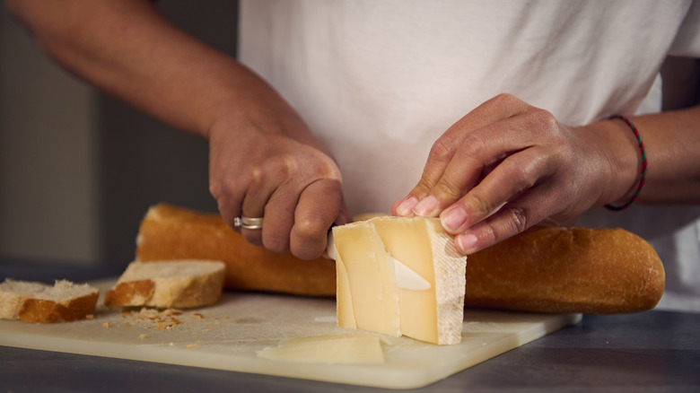 hands slicing cheese with a baguette in the background