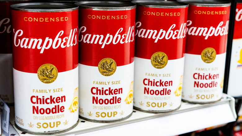 Row of four cans of Campbell's chicken noodle soup on store shelf