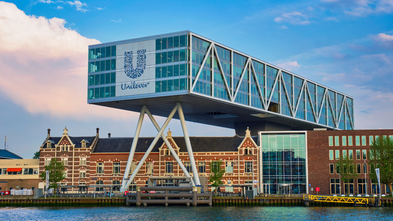 Narrow Unilever office building extends perpendicular over low brick building, upheld by beams, along city waterfront