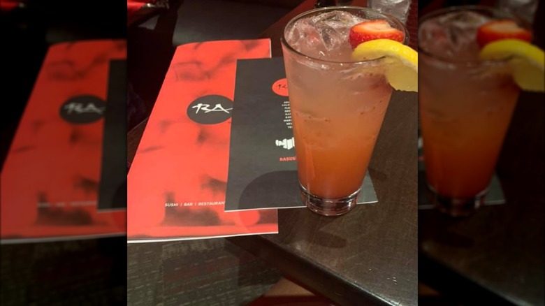 Two red and black RA Sushi menus and a tall drink with a lemon on the rim set on a table.