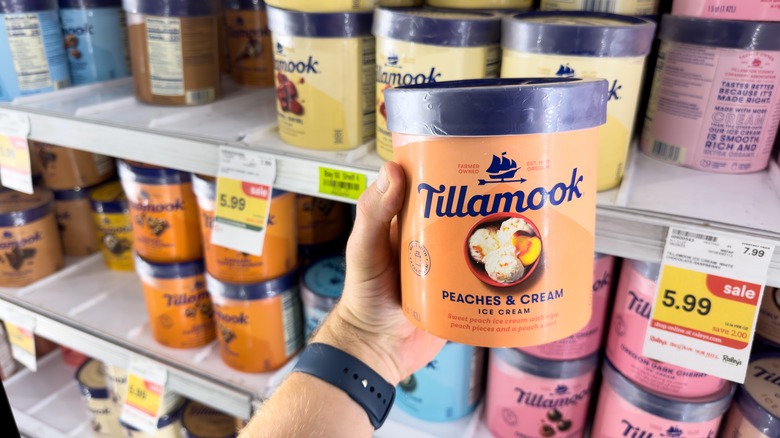 hand holds Tillamook ice cream in front of grocery store display