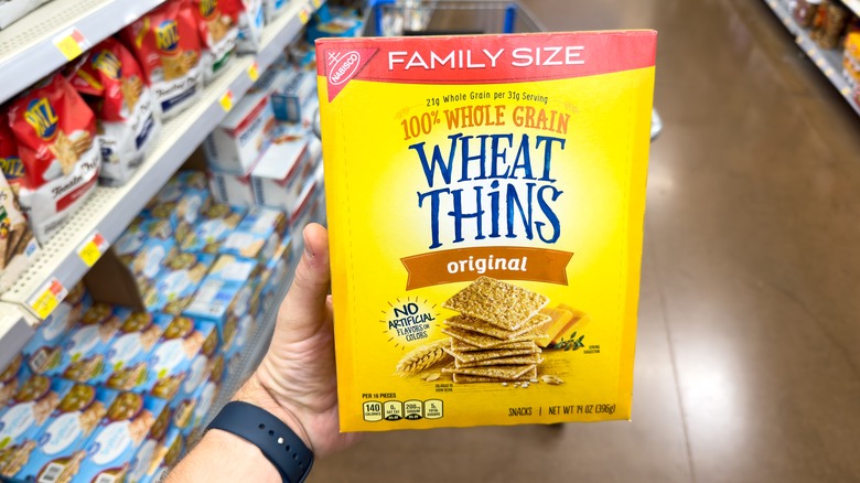 hand holds Nabisco Wheat Thins in grocery store aisle