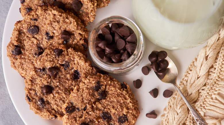 Aerial view of banana, oat, and chocolate chip cookies with jar of chocolate chips and a spoon on a plate.