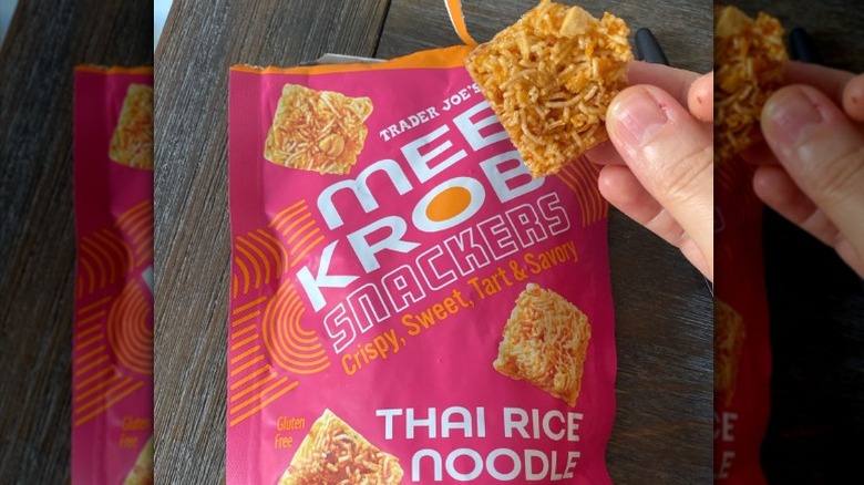 A picture of Trader Joe's Mee Krob Snackers package with someone holding a chip in their hand in front.
