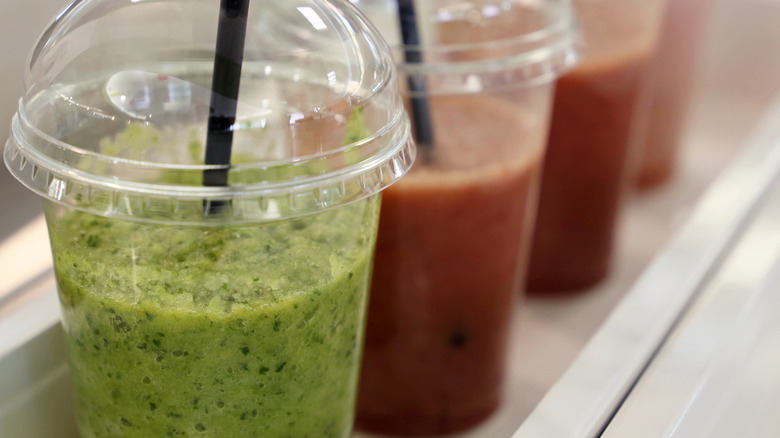 Three store-bought smoothies that are green, pink, and red in plastic to-go cups with black straws