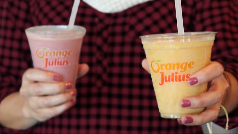 Hands holding two drinks from Orange Julius, a pink one and an orange one
