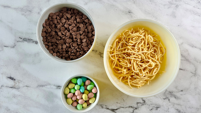 chow mein noodles, chocolate chips, and candy eggs in white bowls