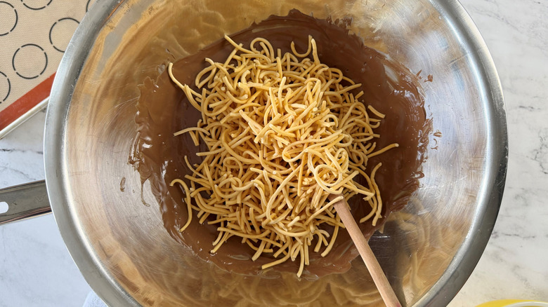 melted chocolate and chow mein noodles in a metal bowl  with a woode