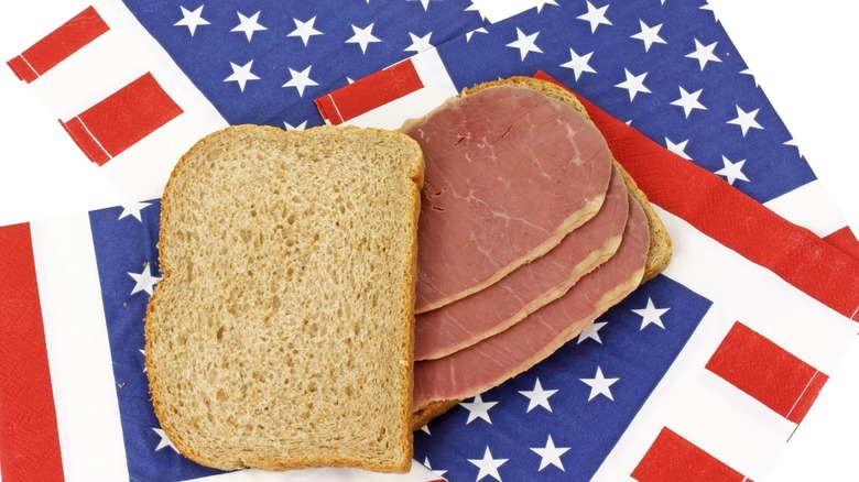A wheat bread corned beef sandwich on several American flag napkins.