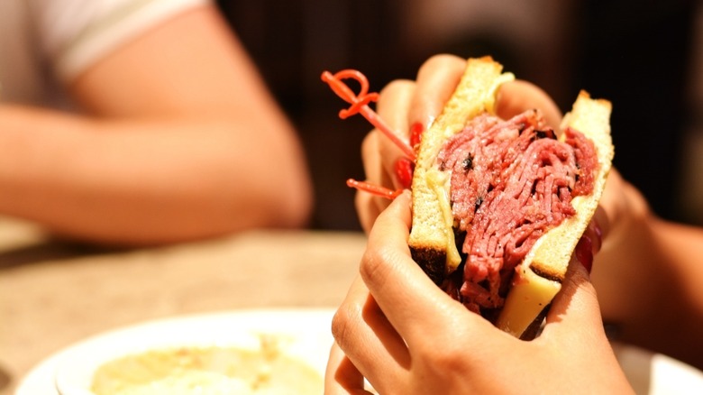 Hands holding a pastrami sandwich