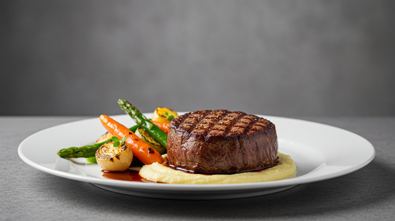 Steak on a bed of mashed potatoes with a side of vegetables on a white plate