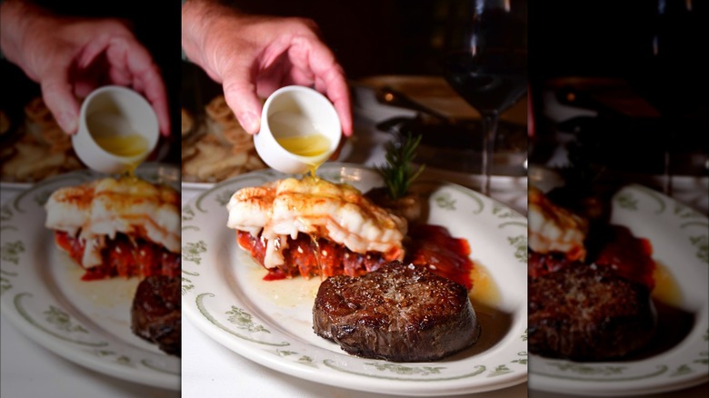 Pouring butter on lobster and steak on a white plate