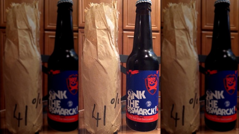 Sink the bismarck beer bottle with blue and red label next to brown paper bag