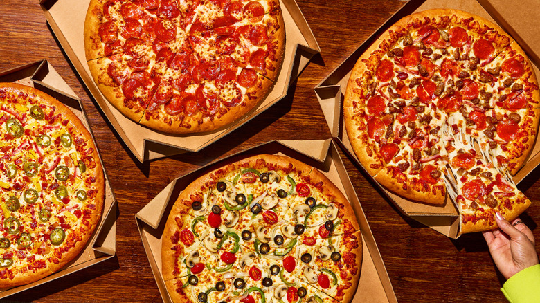 Grabbing a slice from one of four Pizza Hut pizzas on a table