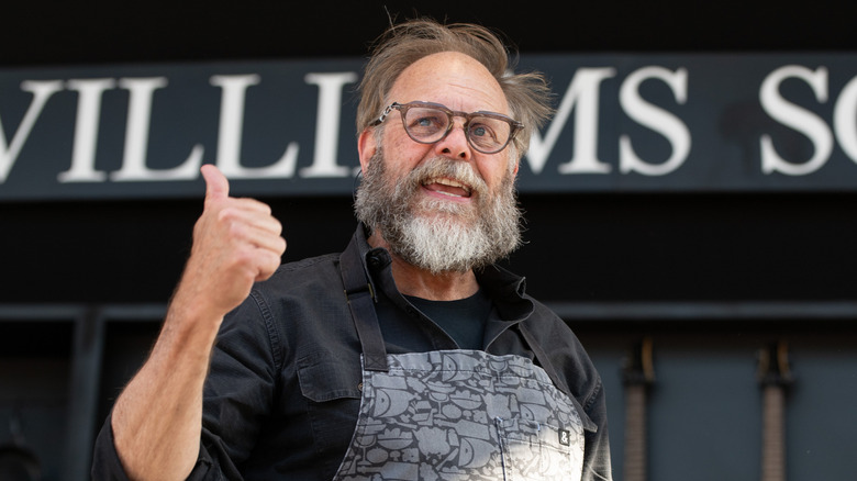 Alton Brown speaking on stage with his thumb up