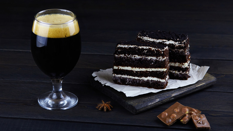 Dark beer in a glass next to chocolate cake and pieces of chocolate.