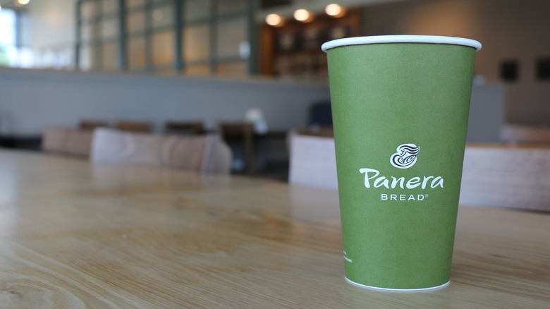 Green Panera drink cup on a wooden table inside the restaurant