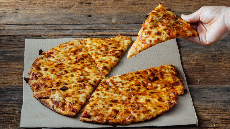 Hand holding slice of thin-crust cheese pizza