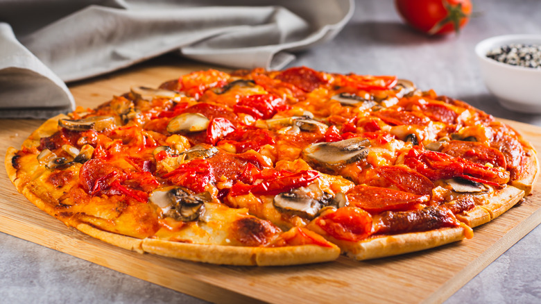 Thin-crust pizza with mushrooms, pepperoni, and red peppers on wooden cutting board