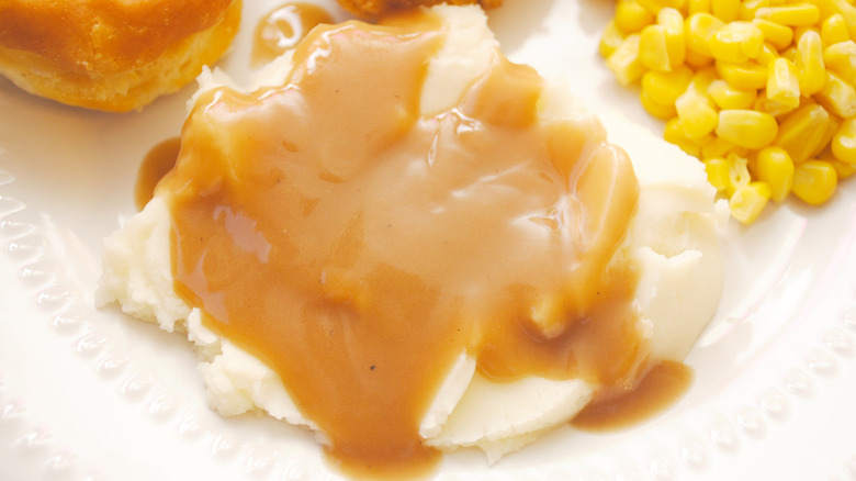 Mashed potatoes and gravy with corn and a biscuit on a white plate