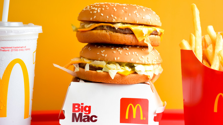 Two McDonald's hamburgers balanced on top of each other on top of a Big Mac container, next to a drink and an order of fries.