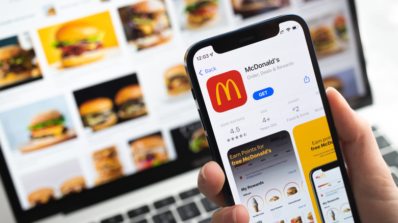 A smartphone showing the McDonald's app, in front of a laptop with various pictures of burgers on the screen.
