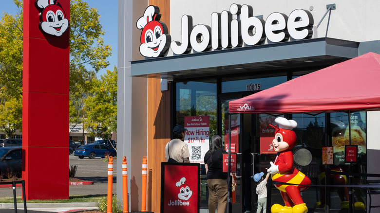 A line extends from the store front of a Jollibee, with a mascot standing out-front.