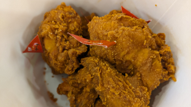 Pieces of spicy chicken from Jollibee rest in a bucket, with red flags sticking out of them.
