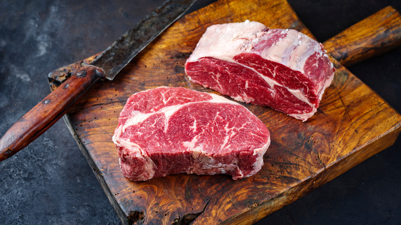Two raw dry-aged Angus steaks on a cutting board, next to a knife