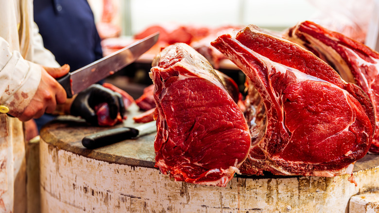 Several cuts of steak on a counter with a butcher's hands cutting one